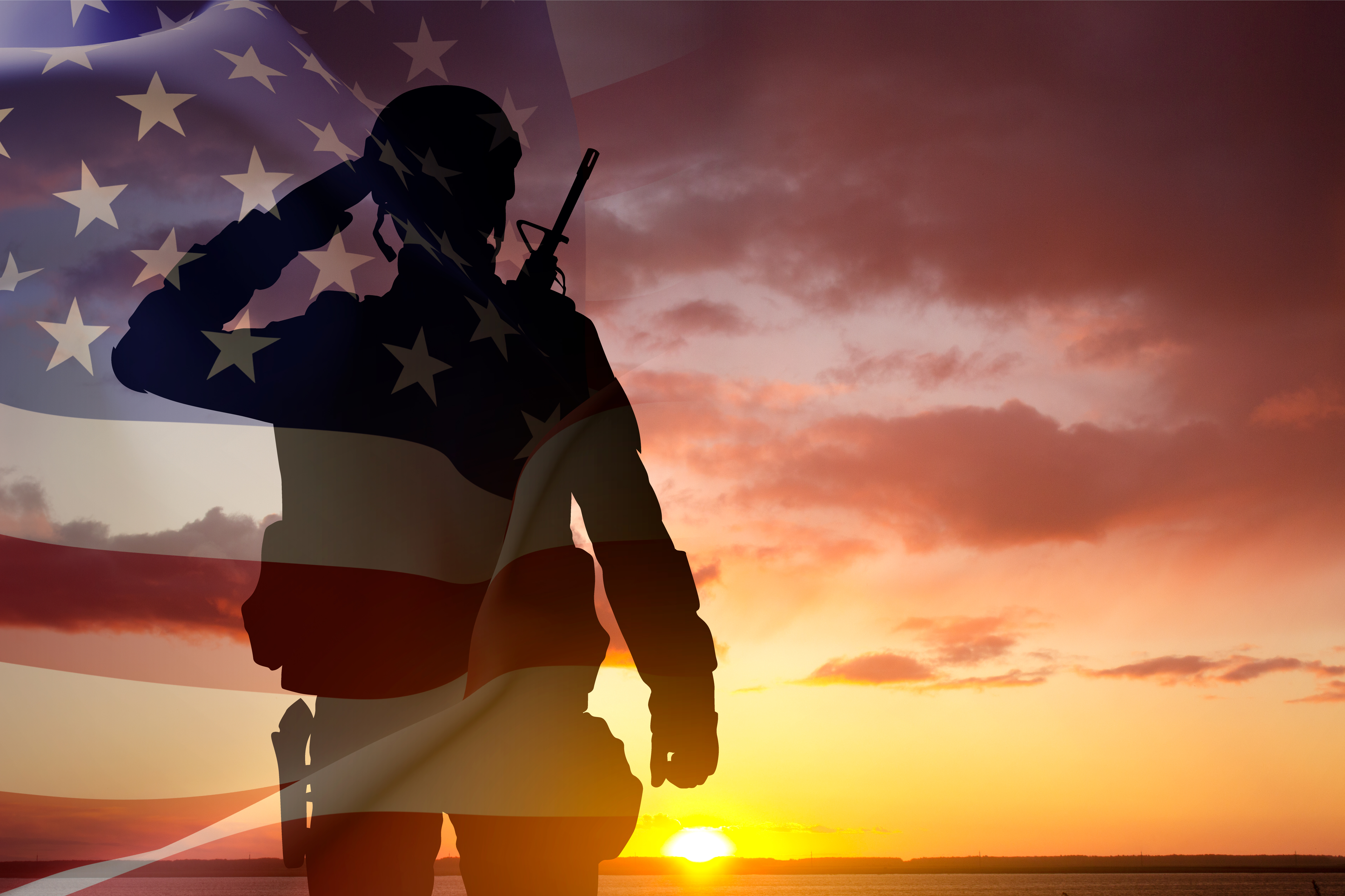 A soldier saluting at sunset with the American flag